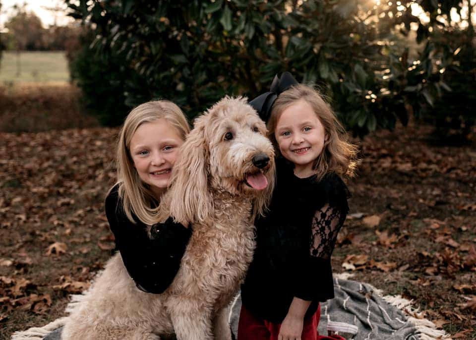 Two girls smiling outdoors with their cheerful pet dog, bringing happiness.